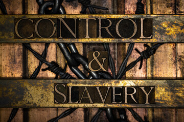 Control and Slavery text over barbed wire and steel chain on vintage textured grunge copper and gold background