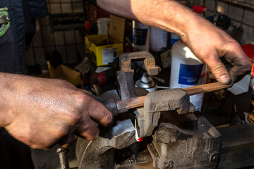 The mechanic uses a metal file to clean the rust-coated brake caliper attached to a bench vise.