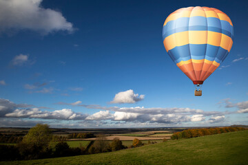 Hot air balloon flying over farmland in rural Hampshire set against blue cloudy sky