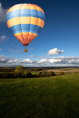 Obraz premium Hot air balloon flying over farmland in rural Hampshire set against blue cloudy sky