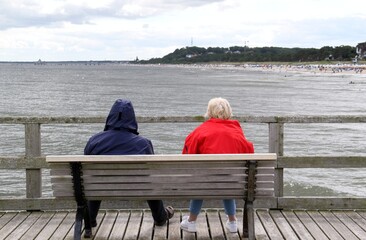 Ehepaar sitztauf einer Bank und schaut auf die Ostsee - 387777368