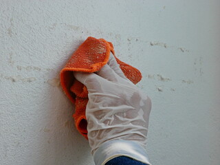 A piece of cloth, soaked with thinner, in a hand of a painter being used to remove sticky rough glue and tape remain on the old concrete wall, as a preparation before starting the paint the house - obrazy, fototapety, plakaty