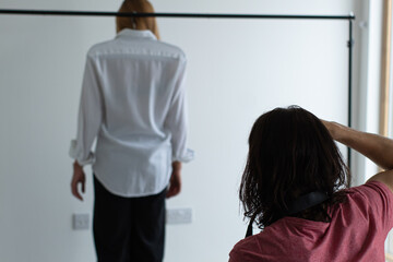 Male photographer taking photos of a blond model that is wearing a white shirt at his photography studio