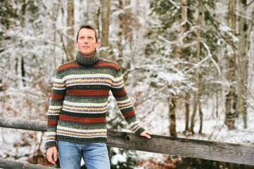 Naklejka na ściany i meble Outdoor winter portrait of middle age man in snowy forest, wearing warm knitted pullover