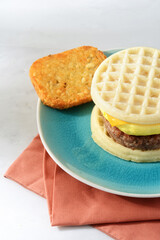 closeup of scrambled egg sausage waffle sandwich with hash brown