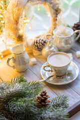 Obraz na płótnie Canvas A cup of English tea with milk from an old mother-of-pearl porcelain service with refined sugar. Christmas tea party breakfast on the background of garlands and fir branches.