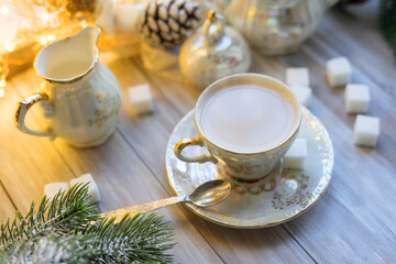 A cup of English tea with milk from an old mother-of-pearl porcelain service with refined sugar. Christmas tea party breakfast on the background of garlands and fir branches.