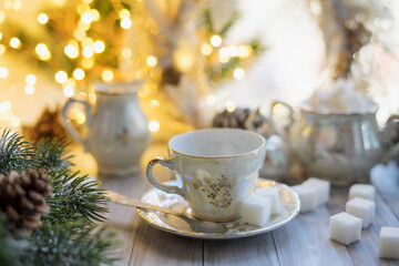 An empty tea cup from an antique mother-of-pearl porcelain set with refined sugar. Christmas tea party breakfast on the background of garlands and fir branches.