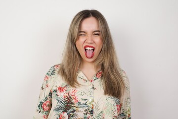 Beautiful caucasian woman with happy and funny face smiling and showing tongue. Wearing casual clothes and standing against white studio background.