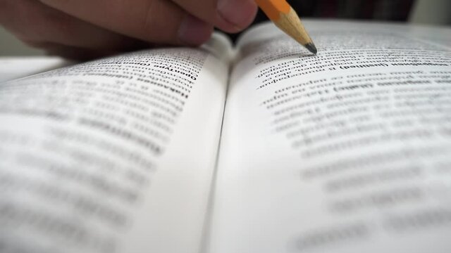Young university student marking the important words from his lectures. Class notebook. Selective focus on example text book. Close up on student hands studying and doing homework.