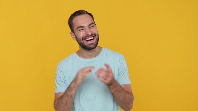 Handsome bearded young guy 20s in basic casual blue t-shirt isolated on yellow background studio. People emotions lifestyle concept. Looking camera smiling laughing applause cheering clapping hands