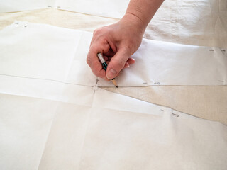 designer's hand draws sketch on calico fabric by pencil according with paper layouts of dress at home
