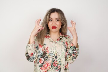 Beautiful young woman holding fingers crossed with worried expression hoping her boss didn't noticed her mistakes at work.