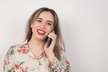 Lifestyle Concept - Portrait of beautiful  young blonde woman standing against white background wearing flowered dress talking on mobile phone with friend.  Copy Space.