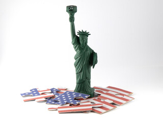 Small replica of the statue of liberty with a puzzle showing the American flag in pieces at her feet in front of white background © Anita_S