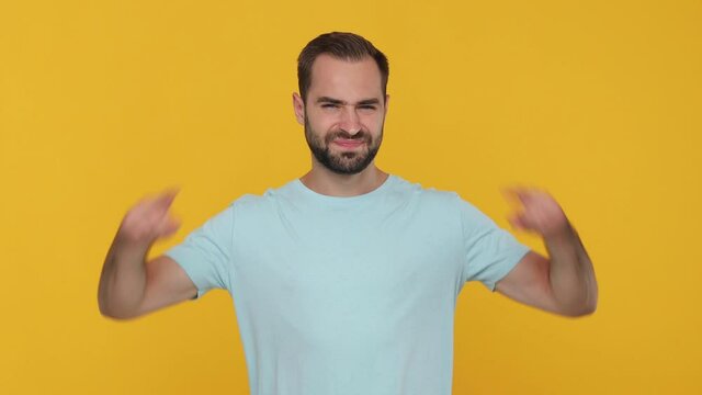 Bearded young man 20s in basic casual blue t-shirt looking at camera covering ears with hands say blah blah do not wanna listen isolated on yellow background studio. People emotions lifestyle concept