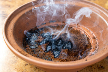 Burning coffee grounds for mosquito and wasp repellent in clay bowl producing burned coffee smoke for  banishing insects.