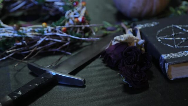 Smooth camera movement and focus change. Close-up of a dagger on the table and a black book with a pentagram. The concept of a witch's table for rituals on the eve of halloween.