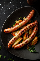 Grilled sausages with fried potatoes, rosemary and basil on a plate