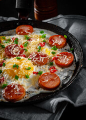 fried eggs with sausage and cheese in a frying pan on wooden table