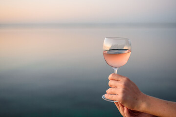 A beautiful glass with pink wine in the hands of a young girl. A glass of wine at sunrise. Romantic breakfast