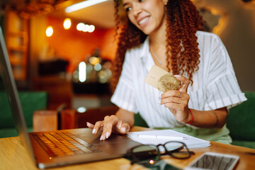 Hands holding credit card and using laptop. Young woman doing online shopping sitting at cafe. Online shopping, e-commerce, internet banking, spending money. Purchases, black friday, discounts, sale.