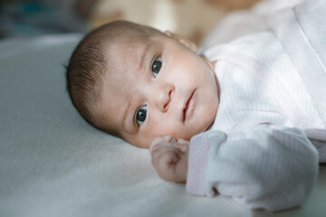 Adorable baby in a white sunny bedroom. Newborn baby is resting in bed. Family morning at home.