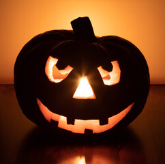 halloween pumpkin with smiling face on fir branches, four teeth. light illuminating the pumpkin from inside