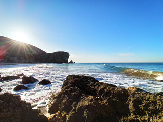 Sea waves crash against rocks on a wild stone beach. Calm sea water. White clouds in the blue sky. sea rest. large stones. foam.
