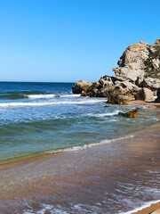Sea waves crash against rocks on a wild stone beach. Calm sea water. White clouds in the blue sky. sea rest. large stones. foam.