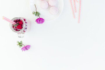 Berries smoothie with straws, marshmallow and anemones flowers on white background. Flat lay