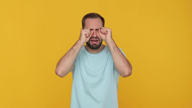 Bearded sad weak fuss young man 20s in basic casual blue t-shirt isolated on yellow background studio. People sincere emotions lifestyle bullying concept. Looking camera crying showing tears on face