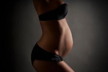 Young pregnant ballerina posing in black lingerie in studio