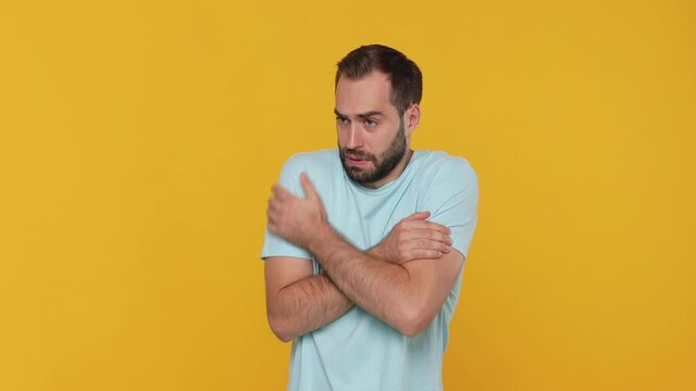 Bearded fun young man 20s in basic casual blue t-shirt isolated on yellow background studio. People lifestyle concept. Look camera rubs his hands froze season feel bad not healthy first signs of cold