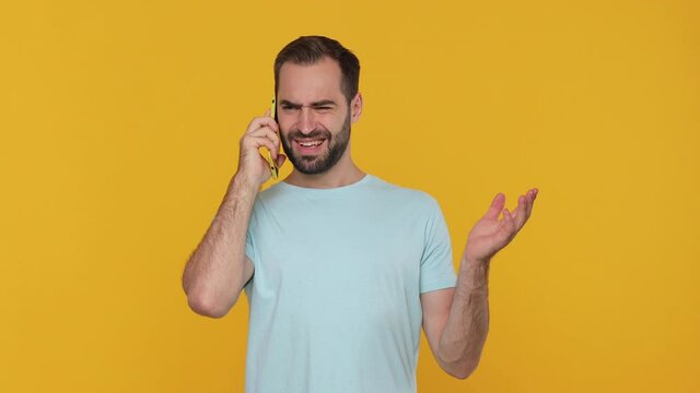 Young man 20s in basic casual blue t-shirt isolated on yellow background in studio. People lifestyle concept. Looking on mobile phone. Doesn't want talk on cellphone showing gesture blah blah ja hand