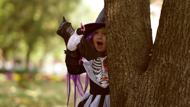 Happy Halloween! A cute little witch with a bat depicts a theater. Beautiful young child girl in suit outdoors.