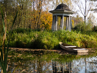 wooden boat on the pond. wooden gazebo on the beach. fallen leaves on the water.