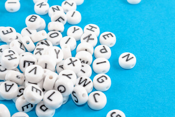 A lot of scattered white small round blocks with black English letters to produce words. Close-up on a blue background.