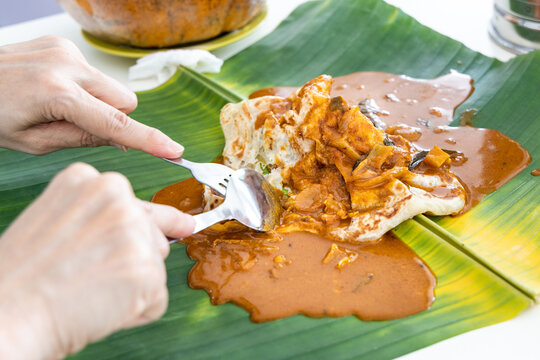 Person Eating Roti Canai Or Paratha Served With Curry Served On Banana Leaf