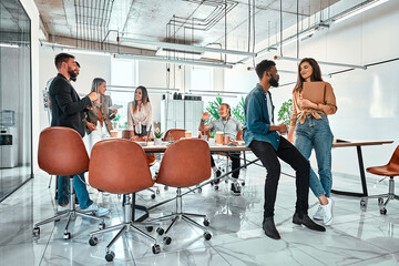 Mixed race successful creative workers collaborate for creating project, sit in coworking space, surrounded with papers and takeaway beverage for having coffee break