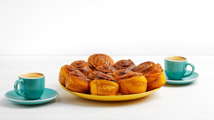 Homemade cinnamon rolls from yeast dough and two cups of coffee espresso on white wooden table. Copyspace.
