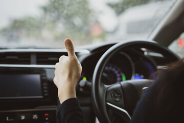 Unrecognizable Asian woman driver showing her thumb up sign during driving a car in the rain