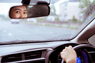 Happy Asian woman looking at the camera via the rear view mirror in a car on the windshield window...