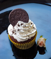 Beautiful creamy white cupcake on black
plate decorated with cookies and a small rose