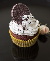 Beautiful creamy white cupcake on black
plate decorated with cookies and a small rose