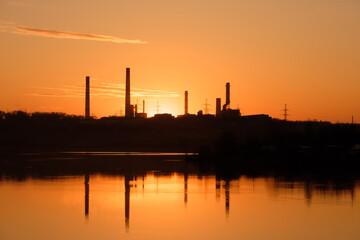 silhouette of factory chimneys on the other side of the river during sunset