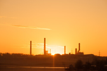 rays of the sun through the factory chimneys during sunset on the shore of the reservoir