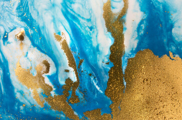 Piles of gold sequins on blue smudges of paint. Abstract pattern.