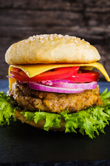 Fresh delicious homemade veggie burger lies on natural slate on rustic wooden background. Delicious tasty burger with lettuce, cheese, onion and tomato. buckwheat and lentil cutlet