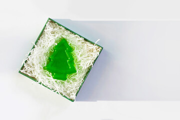 Green box of soap in the shape of green spruce, christmas tree. Open of product in package with white paper filler, top view, shadow. Xmas gift concept, copy space